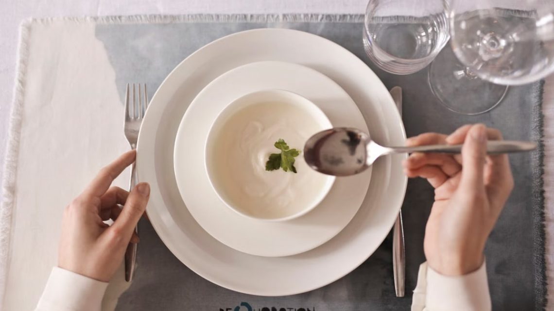 A top-down view of hands ready to enjoy a creamy soup garnished with herbs.