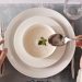 A top-down view of hands ready to enjoy a creamy soup garnished with herbs.