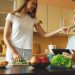 Attractive couple chatting in the kitchen early morning. Beautiful woman feed her husband while cooking breakfast at home