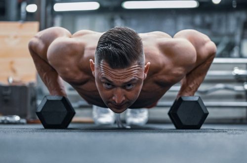 Fit man doing push-ups on hex dumbbells in a modern gym setting.