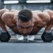 Fit man doing push-ups on hex dumbbells in a modern gym setting.